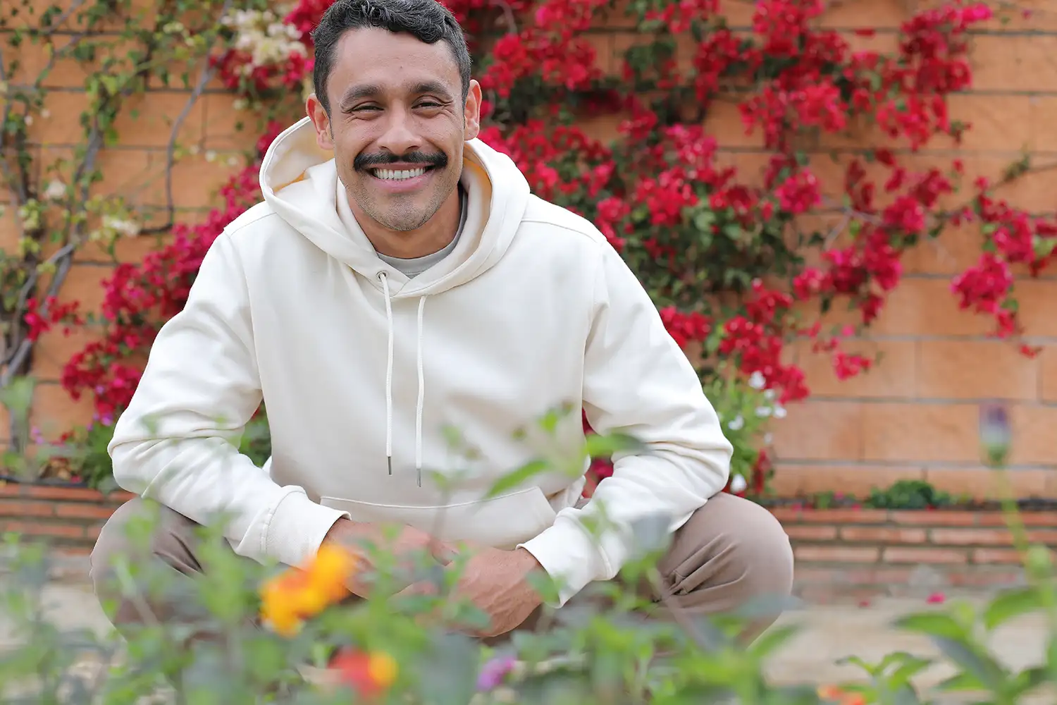 adult man squatting near his garden and smiling with perfect teeth