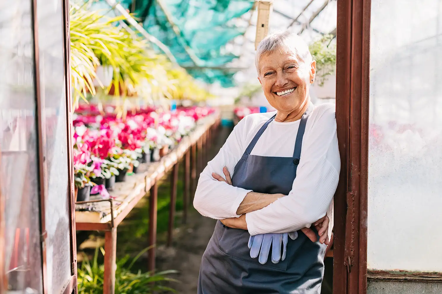 senior woman leaning against her greenhouse and smiling